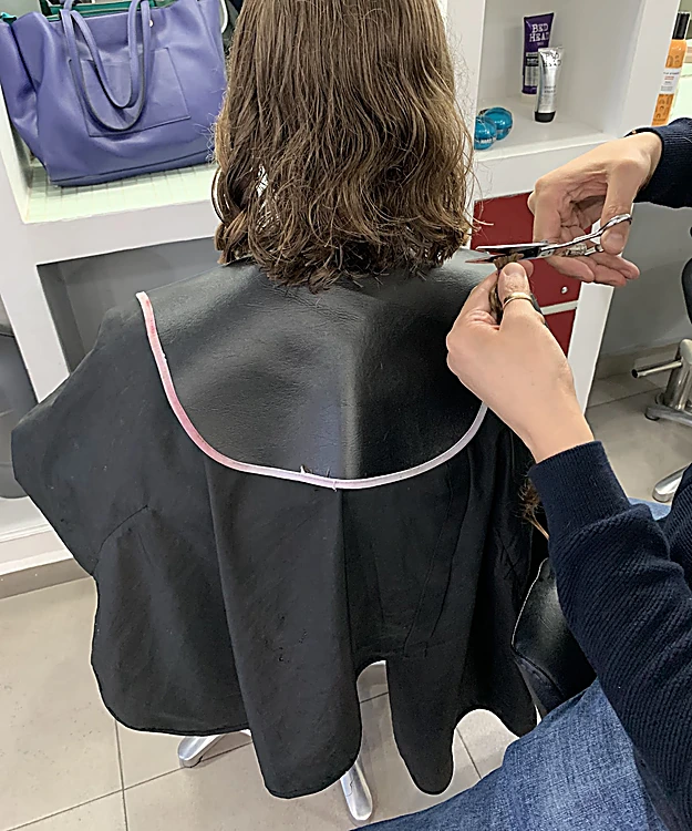 Corte en proceso: tijeras recortando las puntas de una melena castaña
