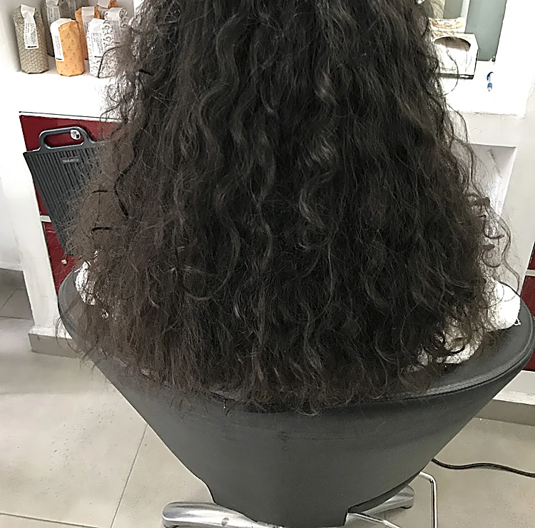 Rizos largos y definidos en pelo oscuro, de espaldas en la silla