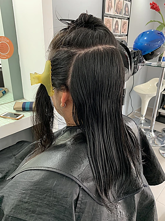 Pelo negro mojado dividido en secciones con una pinza amarilla, antes de aplicar el color